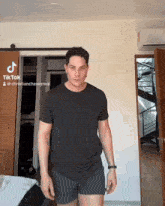 a man in a black shirt and shorts is standing in front of a door with a tiktok icon