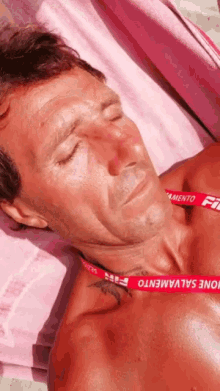 a man is laying on a pink towel with his eyes closed and a red lanyard around his neck that says one salvamento