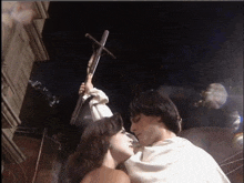 a man holds a cross over a woman 's head as they kiss