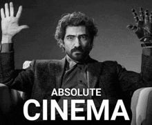 a man in a suit is sitting in a chair with his hands in the air and the words `` absolute cinema '' below him .