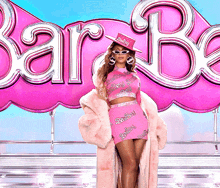 a woman standing in front of a large pink barbie logo