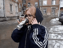 a woman in a hoodie drinking from a can that says ' a ' on it