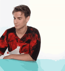 a young man wearing a red and black sweater sits at a table