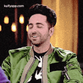 a man wearing a green jacket and a black shirt is smiling .