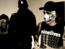 a man wearing a ninelives tank top stands in front of two other people