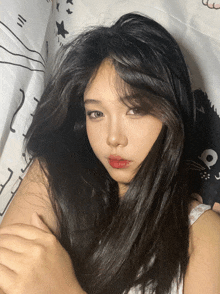 a girl with long black hair and red lips is laying on a bed