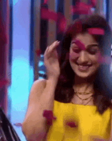 a woman in a yellow dress is smiling and holding a red flower in her hand .