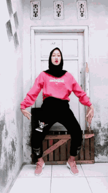 a girl wearing a pink sweatshirt that says ' amanda ' on it sits on a wooden crate