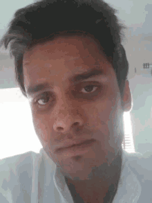 a man in a white shirt is looking at the camera with a serious look on his face