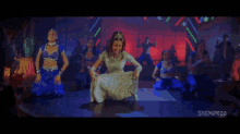 a woman in a white dress is dancing in front of a group of dancers with a watermark that says shemel