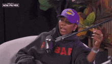 a woman wearing a purple lakers hat talks into a microphone