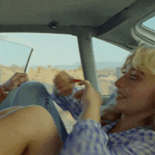 a woman in a plaid shirt is sitting in a car and applying lipstick