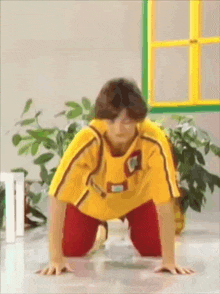 a young boy in a yellow shirt and red pants is doing a handstand on the floor .