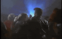a crowd of people are dancing in a dark room with blue lights