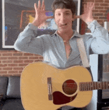 a man in a blue shirt is holding a guitar in front of a brick wall
