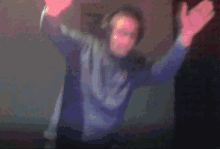 a man wearing headphones is dancing in a dark room with his arms in the air
