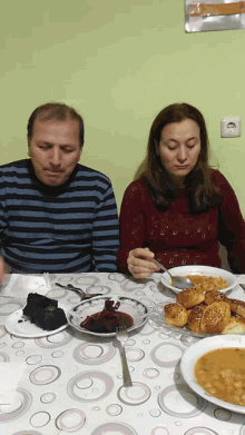 a man and woman sit at a table with plates of food