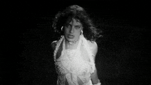 a black and white photo of a woman in a white dress in the dark .