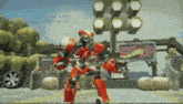 a red robot is standing in front of a sign that says ' hot wheels ' on it .