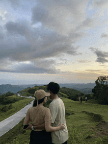 a man and a woman standing on top of a hill looking at a road