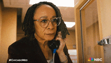 a woman wearing glasses is talking on a phone with the nbc logo in the corner