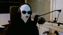 a person wearing a ski mask and headphones holds a microphone