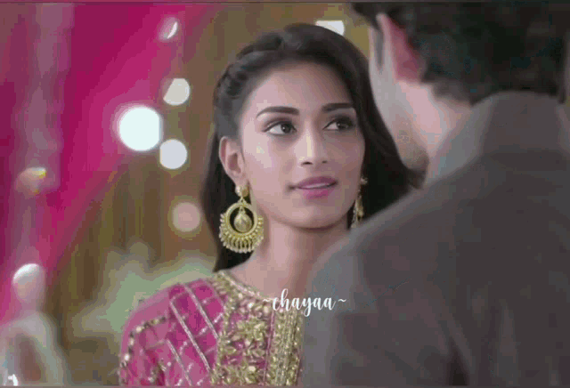 a man and a woman are looking at each other and the woman is wearing a pink dress and gold earrings