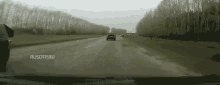 a car is driving down a highway next to a field of trees .