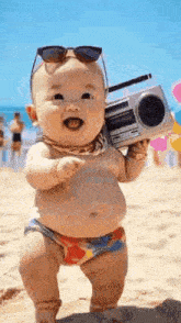 the baby is wearing sunglasses and holding a boombox on the beach .