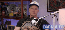 a man in a baseball cap is sitting in front of a microphone with the words dark web on the bottom