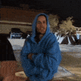 a man in a blue hoodie is standing with his arms crossed in front of a house .