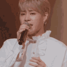 a young man is singing into a microphone while wearing a white shirt with ruffles .