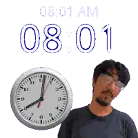 a man stands in front of a wall clock that says 8:01 am