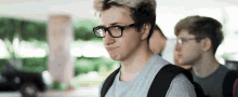 a young man wearing glasses and a backpack looks at the camera
