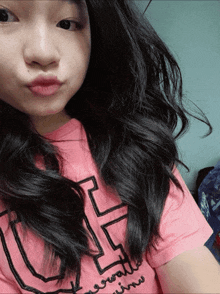 a girl wearing a pink shirt with the letter h on it looks at the camera