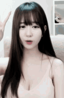 a young woman with long hair and bangs is giving a peace sign .