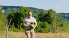 a man is running in a field with a watermelon in his hands .