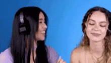 two young women wearing headphones are sitting next to each other on a blue background .