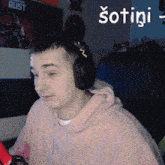 a man wearing headphones and a pink hoodie is sitting in front of a rust poster on the wall