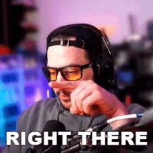 a man wearing headphones and glasses is pointing to his nose with the words right there behind him
