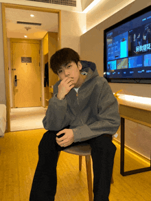 a man sitting on a chair in front of a tv with chinese characters on it