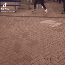 a man in a blue shirt is dancing on a brick sidewalk in front of a crowd .