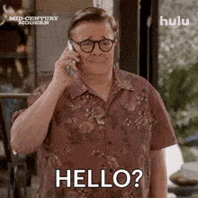 a man in a floral shirt is talking on a cell phone and has the word hello written on his face