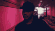 a man wearing a black hat and sunglasses stands in a hallway