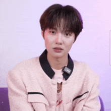 a young man wearing a pink jacket and a necklace is smiling .