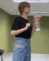 a woman in a black shirt and blue jeans is holding a bottle of water
