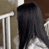a woman with long black hair is standing next to a railing and looking at the camera .