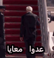 a man in a suit is walking down a set of red stairs with arabic writing behind him