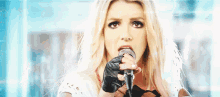 a blonde woman is singing into a microphone with gloves on her hands