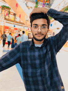 a man wearing glasses and a plaid shirt holds his head